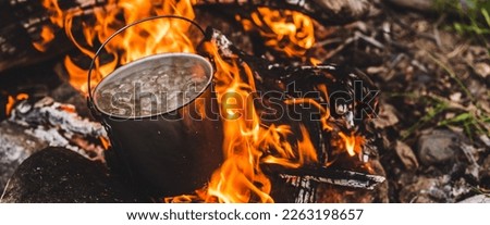 Kettle stands on fire. Cooking food at fire in wild. Beautiful big log burns in bonfire close-up. Survival in wild nature. Wonderful flame with caldron. Pot is on flames. Campfire background.