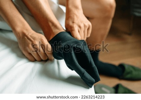 closeup of a man putting on a compression sock sitting on the edge of his bed at home