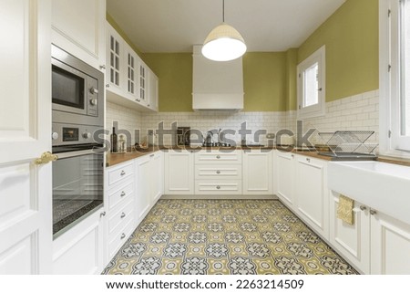 Vintage-style kitchen furnished in a u-shaped white lacquered wood with wooden countertop, white tiles and hydraulic tile floor Royalty-Free Stock Photo #2263214509