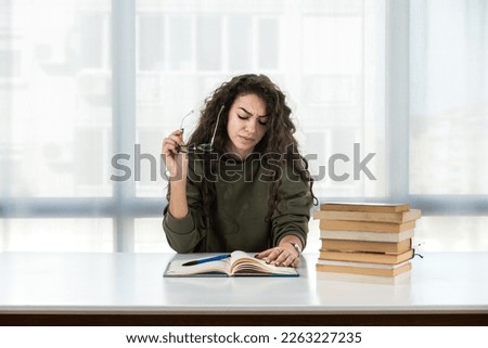 Young girl future law or economics student feeling nervous and anxious because she has a lot to study for her college entrance exam sitting with a pile of books on the table and has a headache Royalty-Free Stock Photo #2263227235