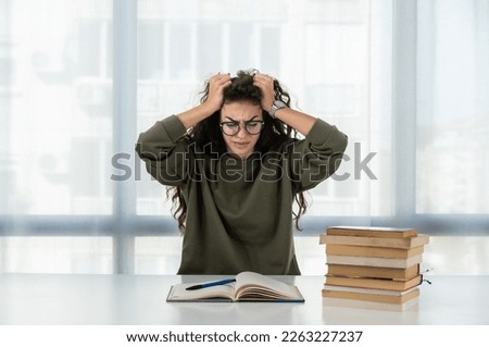 Young girl future law or economics student feeling nervous and anxious because she has a lot to study for her college entrance exam sitting with a pile of books on the table and has a headache Royalty-Free Stock Photo #2263227237