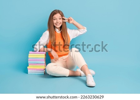 Full length photo of pretty lovely lady sitting floor empty space v-sign near eye promoting literature isolated on blue color background