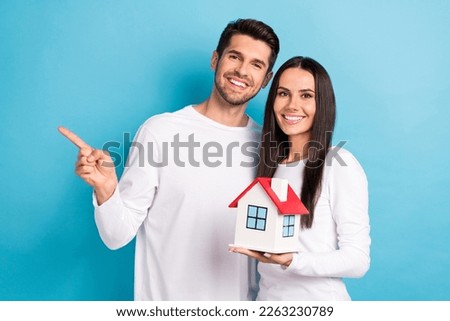 Portrait of two cheerful satisfied persons dressed white shirts directing empty space hold small house isolated on blue color background