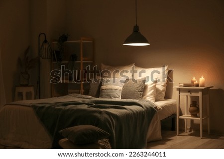 Interior of bedroom with green blankets on bed, burning candles and glowing lamp at night Royalty-Free Stock Photo #2263244011