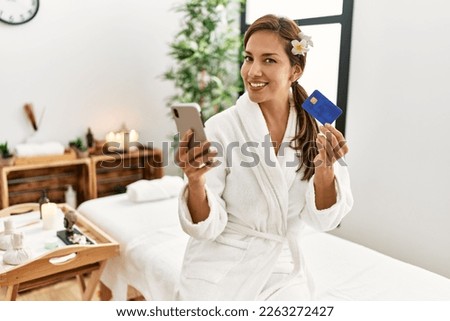 Young latin woman wearing bathrobe using smartphone and credit card 
