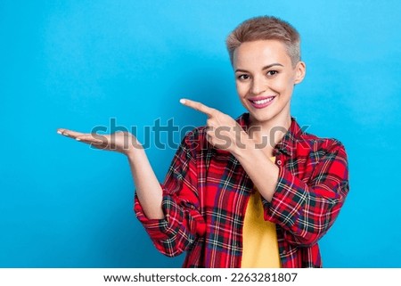 Photo of cheerful positive cute girl with short hairstyle dressed red shirt directing empty space isolated on blue color background