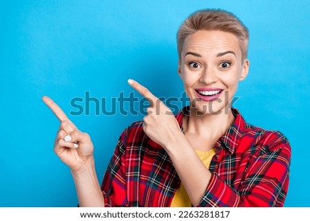 Portrait of young funny surprised woman short blonde hairdo wear plaid red shirt direct fingers mockup crazy offer isolated on blue color background