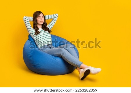 Full size photo of pleasant peaceful woman curly hairstyle striped sit on armchair arms behind head isolated on yellow color background