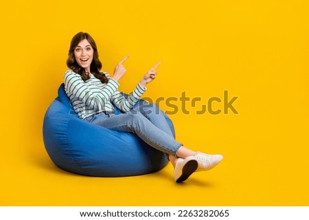 Full size photo of cheerful nice woman curly hairstyle striped sit on bean bag indicating empty space isolated on yellow color background