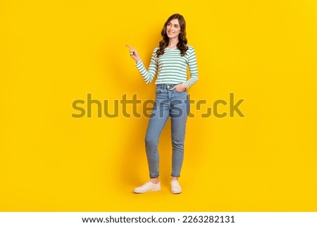Full size photo of cute woman curly hairstyle striped shirt arm in pocket directing look empty space isolated on yellow color background