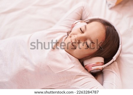 Adorable hispanic girl listening to music lying on bed at bedroom Royalty-Free Stock Photo #2263284787