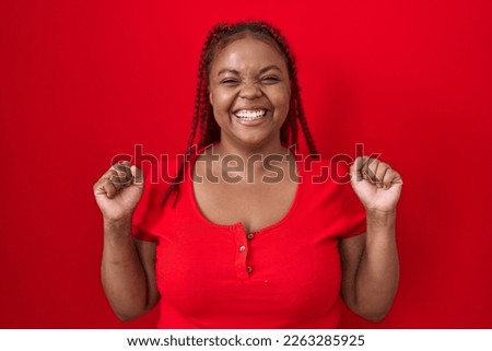African american woman with braided hair standing over red background celebrating surprised and amazed for success with arms raised and open eyes. winner concept. 