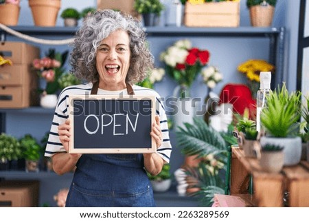 Middle age woman with grey hair working at florist with open sign smiling and laughing hard out loud because funny crazy joke.  Royalty-Free Stock Photo #2263289569