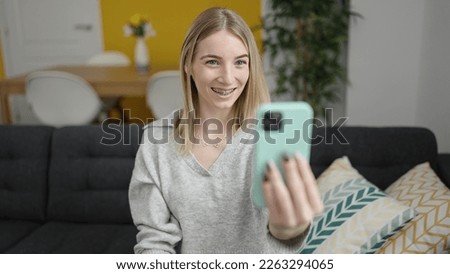 Young blonde woman taking selfie picture with smartphone sitting on the sofa at home