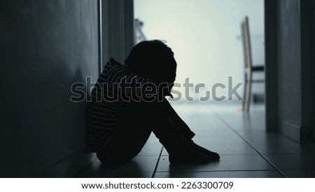 Sad child suffering from depression sitting alone in corridor feeling loneliness. Scared fearful small boy covering face in silhouette at home Royalty-Free Stock Photo #2263300709