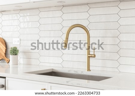 A beautiful kitchen faucet detail with white cabinets, a gold faucet, white marble countertops, and a brown picket ceramic tile backsplash. Royalty-Free Stock Photo #2263304733