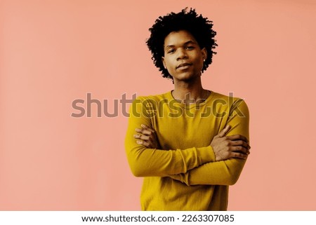An adult stands with arms crossed, sporting curly hair in a unique hairstyle. Studio shot portrait, copy space.