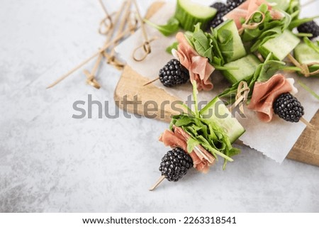Salad skewers - prosciutto, blackberries, cucumber and arugula on board; fruit, vegetable and meat bite size party appetizers Royalty-Free Stock Photo #2263318541