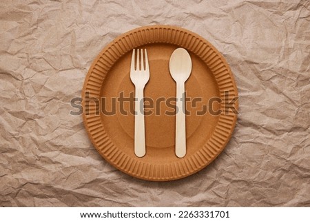 Wooden fork, spoon on cardboard plate on crumpled paper background