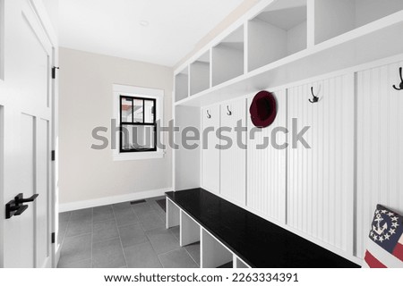 A white mud room foyer with a dark grey tile floor, white shelving, coat hooks, and wood bench seat. Royalty-Free Stock Photo #2263334391