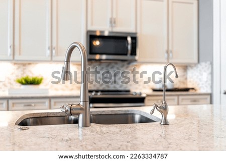 New modern faucet and kitchen sink closeup with island and granite countertops with bokeh background of microwave and oven stove with bright white cabints and nobody Royalty-Free Stock Photo #2263334787