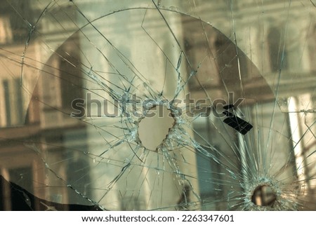 A hole in the window glass with a bullet during a military shooting. Cracks propagate around the hole. Dirty window frame. View of the street from the inside.