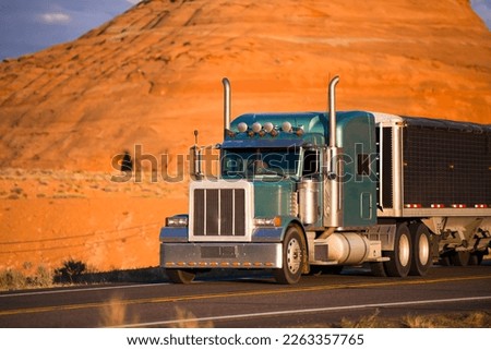 Classic green big rig semi truck with storage compartment and tall exhaust pipes running with special designed low bulk covered semi trailer transporting cargo on the desert road in Page Arizona Royalty-Free Stock Photo #2263357765