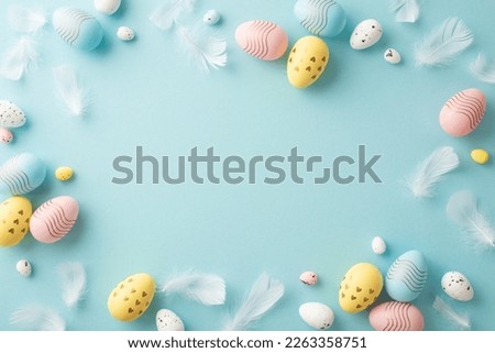 Easter decorations concept. Top view photo of colorful easter eggs and blue feathers on isolated pastel blue background with empty space in the middle