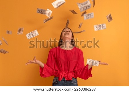 Happy young woman under money rain on orange background. Girl throwing money. Big profit or win lottery concept