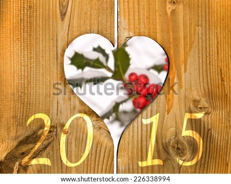 2015, wooden frame in the shape of a heart and branch of holly under the snow in the background