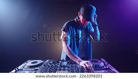 Cool hipster disc jockey performing in a nightclub at a mixer controller, spotted by colorful lights on smoked black background - nightlife concept  Royalty-Free Stock Photo #2263398201