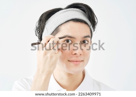 Asian man drawing eyebrows with an eyebrow pencil in white background Royalty-Free Stock Photo #2263409971
