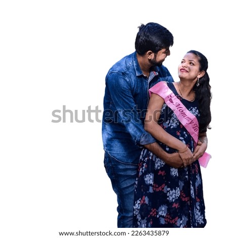 Indian couple posing for maternity baby shoot with white plain background. The couple is posing in a lawn with green grass and the woman is falunting her baby bump in Lodhi Garden in New Delhi, India