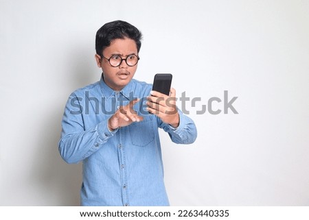 Portrait of shocked Asian man in blue shirt looking at mobile phone. Wow face expression. Isolated image on white background
