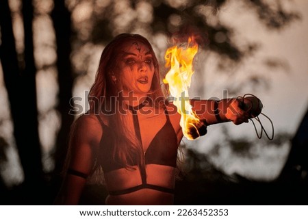 Girl fire dancing performance at outdoor art festival, smooth movements of female fire show artist with torch. Woman dancing with fire flame art performance, twilight forest background