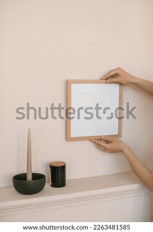 Woman hanging blank photo frame with empty copy space on beige wall. Close-up, mockup. Artwork showcase. Royalty-Free Stock Photo #2263481585
