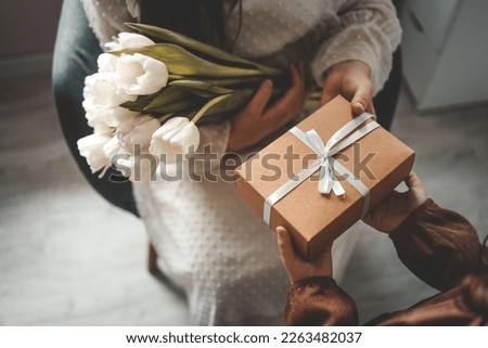 The child's hands hold a beautiful gift box with a ribbon and white tulips. Top view, close-up. Happy mother's day. Royalty-Free Stock Photo #2263482037