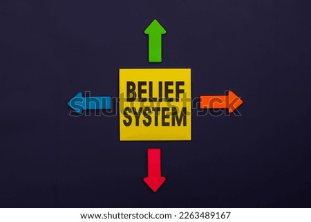 BELIEF SYSTEM - inscription of a yellow paper note next to an four colorful arrows over a dark blue background. Business, tips and tricks concept