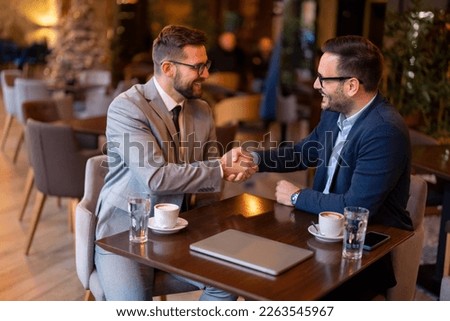 Two smiling confident male business partners at business meeting in restaurant shaking hands as sign they have reached an agreement, finishing up a meeting or setting goals, sharing productive ideas.