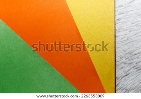 A bundle of high-quality colored paper lies on a white background. Three-color geometric surface, orange, yellow and green