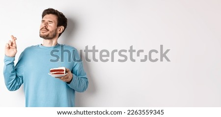 Celebration and holidays concept. Handsome young man celebrating birthday, making wish with bday cake in hand, standing over white background.