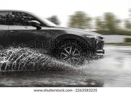Black car driving through puddle at high speed on rainy day, motion blur effect Royalty-Free Stock Photo #2263583235