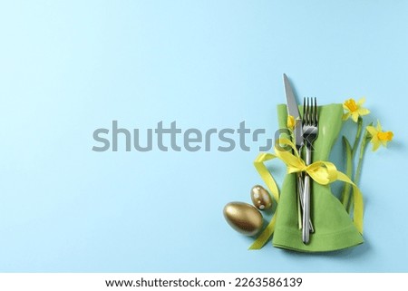 Cutlery set, Easter eggs and narcissuses on light blue background, flat lay with space for text. Festive table setting