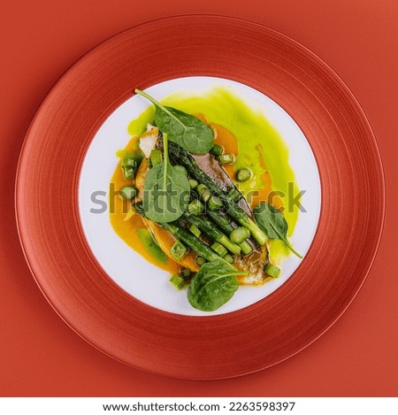 Fish dish - fried cod fillet with asparagus and basil served on red plate