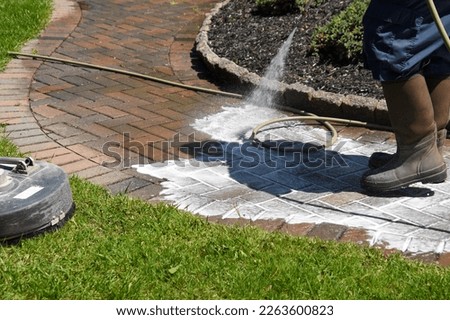 Rubber waterproof boots seen near where a workman is spraying detergent on a dirty brick sidewalk