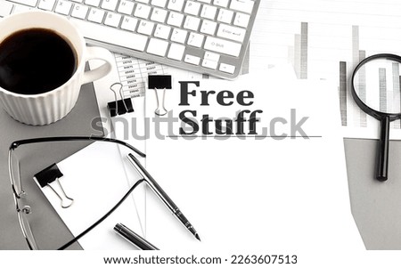 FREE STUFF text on a paper with magnifier, coffee and keyboard on a grey background