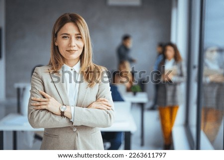 Successful businesswoman standing in creative office and looking at camera. Woman entrepreneur in a coworking space smiling. Portrait of beautiful business woman standing in front of business team Royalty-Free Stock Photo #2263611797