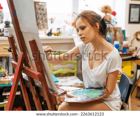 Close-up photo of a female artist in her studio reflects on her work. She thoughtfully looking at her artwork. Creativity as a psychological relief and release from stress.
