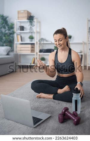 Fitness coach live streaming on laptop while sitting on the floor at home