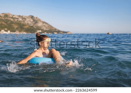 Cheerful girl sits in an inflatable circle and splashes with water in the sea Royalty-Free Stock Photo #2263624599